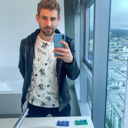 Nick Viall in a white t-shirt and blue hood poses for a mirror selfie.